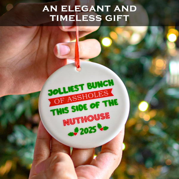 Hand holding a Christmas ornament with humorous text against a blurred Christmas tree background.