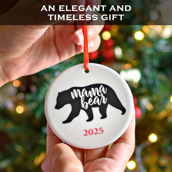Ornament with 'mama bear' design held in front of a decorated Christmas tree.