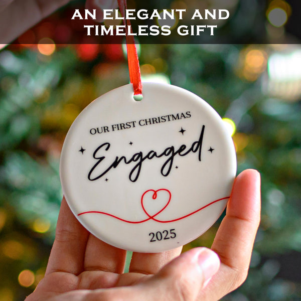 Decorative ornament with 'Our First Christmas Engaged 2025' text held in front of a blurred Christmas tree.