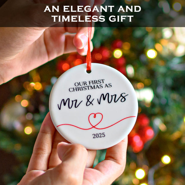 Decorative ornament with 'Our First Christmas as Mr & Mrs 2025' text held in front of a festive tree.
