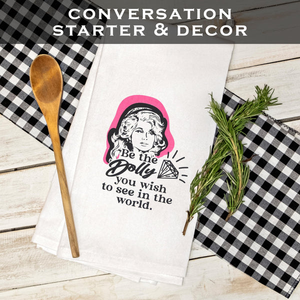 Towel with Dolly Parton quote, wooden spoon, and rosemary on checkered fabric