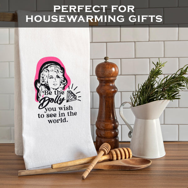 Tea towel with a graphic design of a woman and text, placed on a kitchen counter with utensils and decor.
