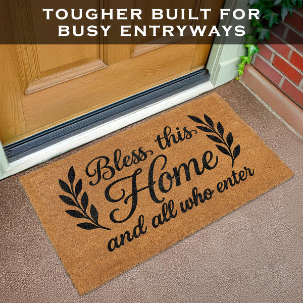 Doormat with 'Bless this Home and all who enter' text on a carpeted floor in front of a door.