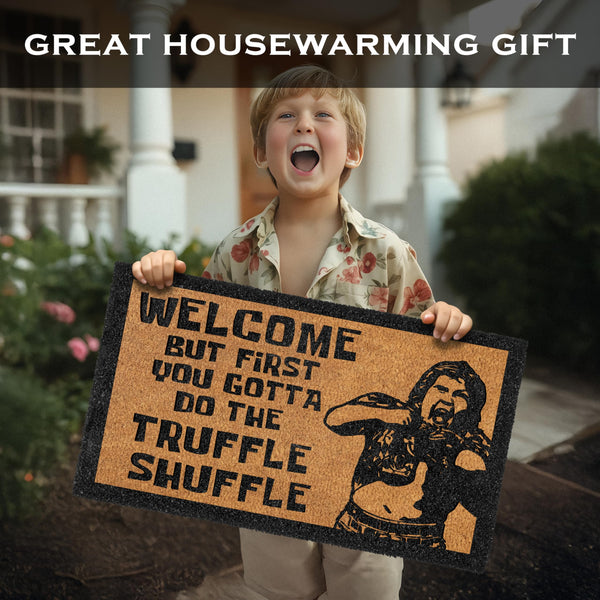 Child holding a doormat with a humorous design and text, set against a house exterior.