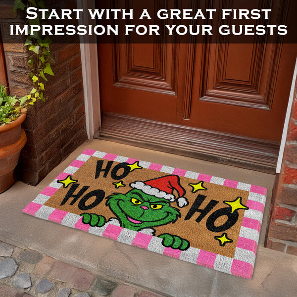 Decorative doormat with Grinch design and text 'HO HO HO' on a stone porch.