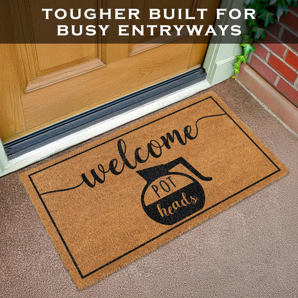 Doormat with 'welcome pot heads' text on a carpeted floor in front of a door.