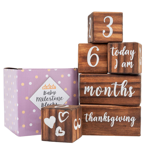 A set of wooden blocks with numbers and words printed on them, used as a baby milestone prop, displayed alongside its packaging box.