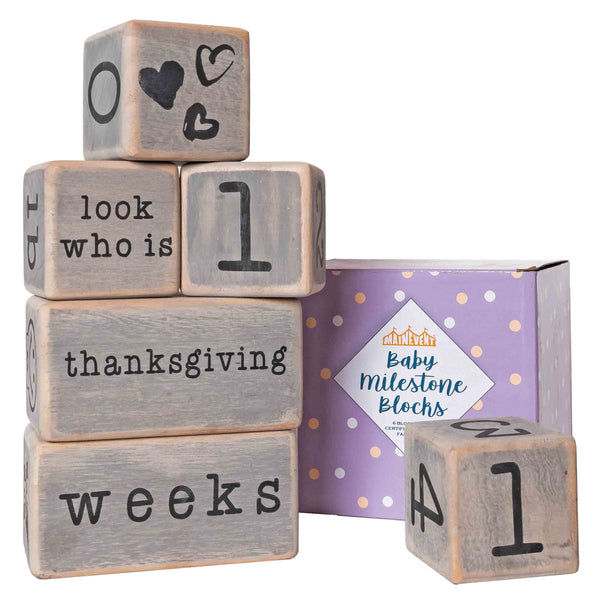 A set of wooden blocks with numbers and words printed on them, used as a baby milestone prop, displayed alongside its packaging box.