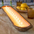 Long wooden candle holder with multiple candles on a table with lemons and a glass.