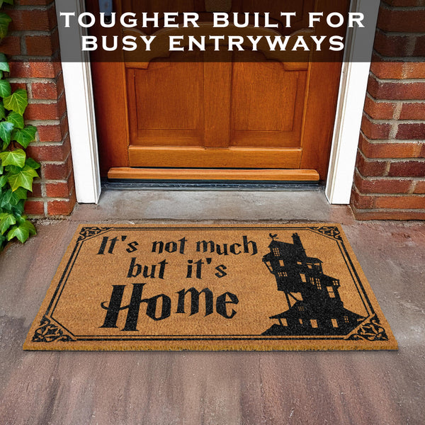 Doormat with 'It's not much but it's Home' text in front of a wooden door.