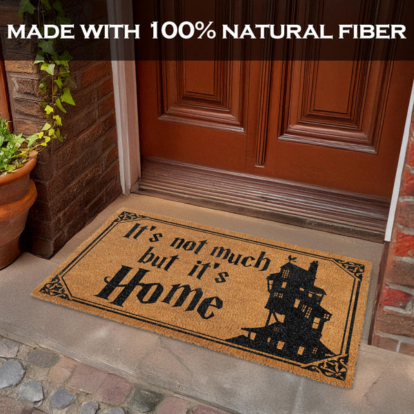 Doormat with 'It's not much but it's Home' text and house illustration on a stone porch.