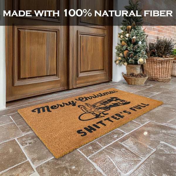 Doormat with Christmas design on a stone floor in front of wooden doors, with text 'Made with 100% natural fiber'.